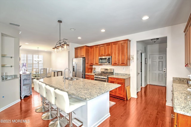 kitchen with light stone counters, a breakfast bar, decorative light fixtures, appliances with stainless steel finishes, and a sink