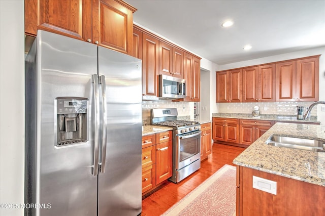 kitchen featuring brown cabinetry, light stone counters, stainless steel appliances, light wood-style floors, and a sink