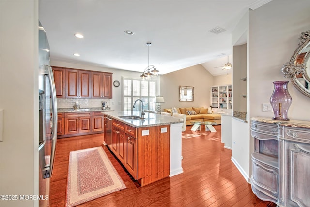 kitchen featuring brown cabinets, stainless steel appliances, open floor plan, a sink, and an island with sink