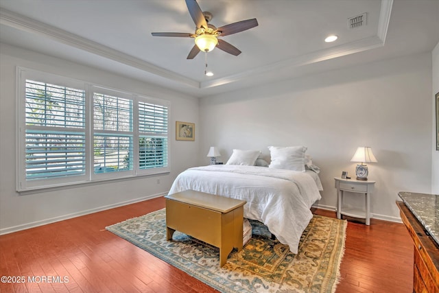 bedroom featuring baseboards, a raised ceiling, dark wood finished floors, and ornamental molding