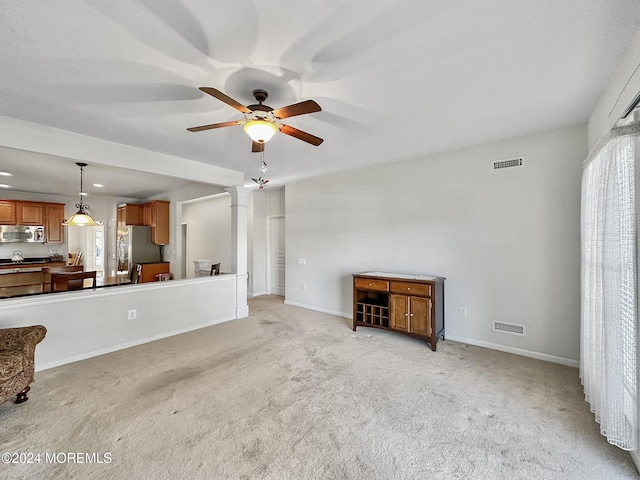 unfurnished living room featuring light colored carpet, ornate columns, and ceiling fan