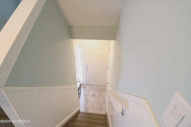 stairs featuring a wainscoted wall, vaulted ceiling, and wood finished floors