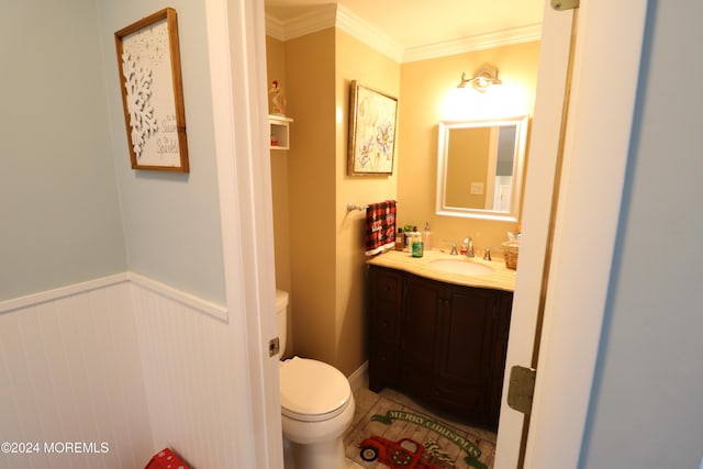 half bathroom with toilet, vanity, wainscoting, tile patterned floors, and crown molding