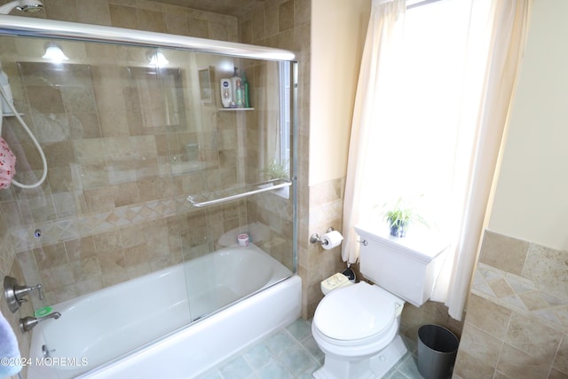 bathroom featuring toilet, shower / bath combination with glass door, and tile walls