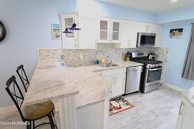 kitchen featuring a peninsula, a sink, appliances with stainless steel finishes, light stone countertops, and tasteful backsplash