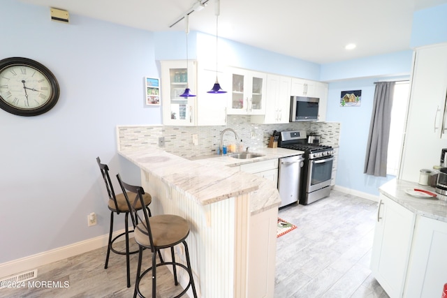 kitchen featuring decorative backsplash, appliances with stainless steel finishes, a kitchen breakfast bar, a peninsula, and a sink