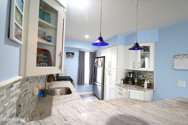 kitchen with a sink, white cabinets, freestanding refrigerator, decorative backsplash, and glass insert cabinets