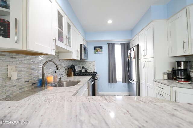 kitchen featuring glass insert cabinets, appliances with stainless steel finishes, light stone countertops, white cabinetry, and backsplash