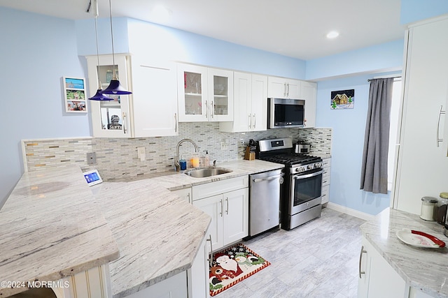 kitchen featuring tasteful backsplash, white cabinets, appliances with stainless steel finishes, light stone countertops, and a sink