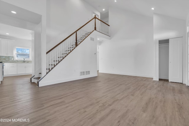 unfurnished living room with a towering ceiling, sink, and light hardwood / wood-style flooring