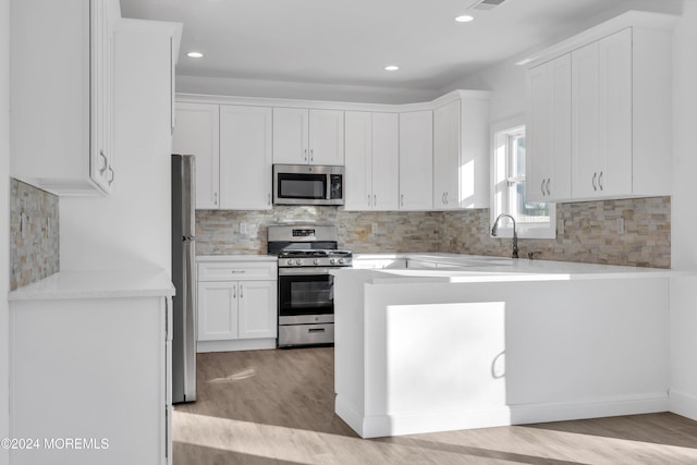 kitchen with white cabinets, appliances with stainless steel finishes, light wood-type flooring, and decorative backsplash