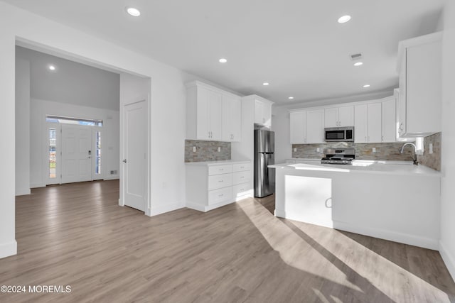 kitchen featuring decorative backsplash, appliances with stainless steel finishes, light wood-type flooring, and white cabinetry