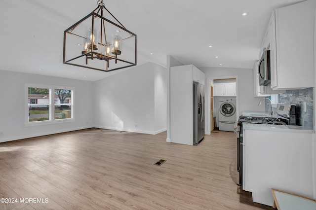 kitchen with appliances with stainless steel finishes, light hardwood / wood-style flooring, washer / clothes dryer, white cabinetry, and lofted ceiling