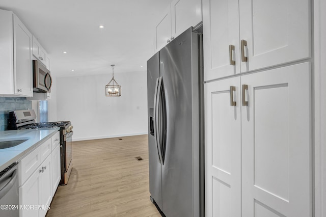 kitchen with backsplash, white cabinets, light hardwood / wood-style flooring, appliances with stainless steel finishes, and light stone counters