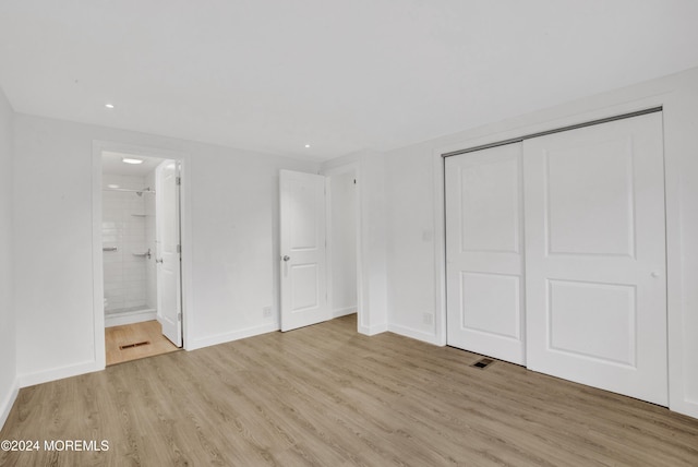 unfurnished bedroom featuring a closet, light wood-type flooring, and ensuite bath