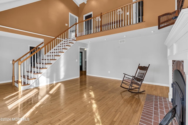 unfurnished living room with a high ceiling, a brick fireplace, and wood-type flooring