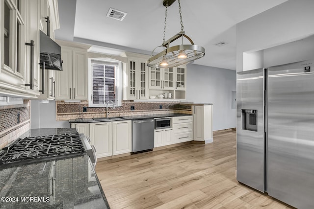 kitchen featuring decorative light fixtures, light wood-type flooring, appliances with stainless steel finishes, white cabinets, and backsplash