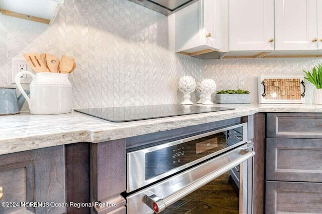 kitchen featuring stainless steel oven, light stone counters, black electric cooktop, dark brown cabinets, and white cabinets