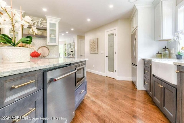 kitchen featuring backsplash, white cabinets, light stone countertops, light hardwood / wood-style floors, and stainless steel appliances