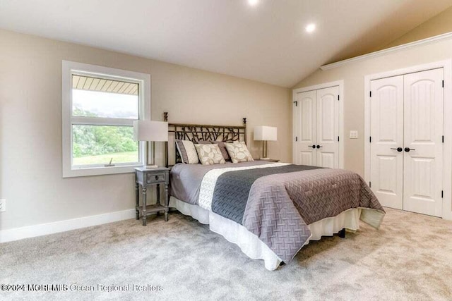 bedroom with two closets, light colored carpet, and vaulted ceiling