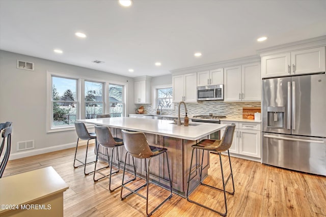 kitchen with white cabinets, appliances with stainless steel finishes, light wood-type flooring, and a center island with sink