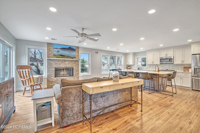 living room featuring a stone fireplace, a wealth of natural light, light hardwood / wood-style flooring, and ceiling fan