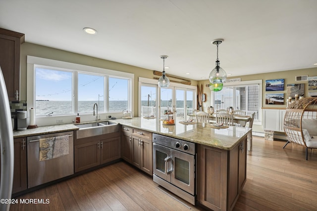 kitchen with light stone countertops, sink, pendant lighting, a water view, and appliances with stainless steel finishes