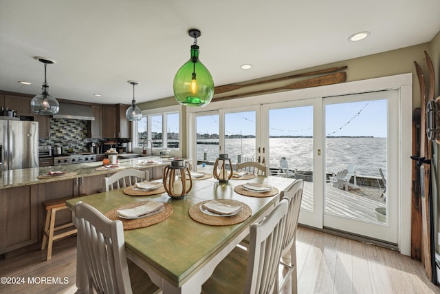 dining space featuring sink, french doors, a water view, and light wood-type flooring