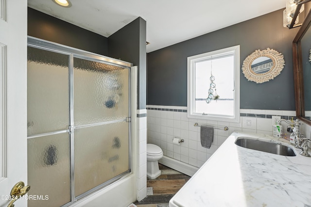 full bathroom featuring vanity, shower / bath combination with glass door, hardwood / wood-style flooring, toilet, and tile walls