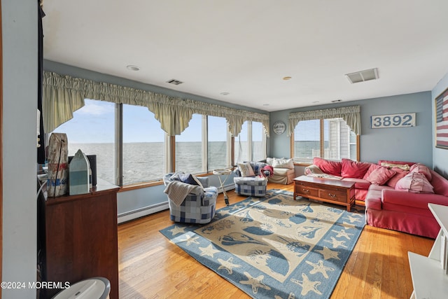 living room featuring a water view, light hardwood / wood-style flooring, baseboard heating, and a healthy amount of sunlight