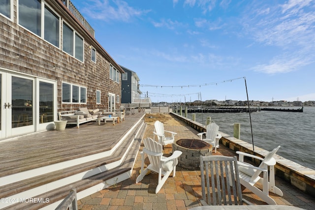 exterior space featuring a deck with water view and an outdoor living space with a fire pit