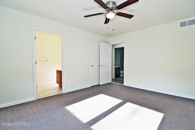 unfurnished bedroom featuring ensuite bath, ceiling fan, and dark colored carpet