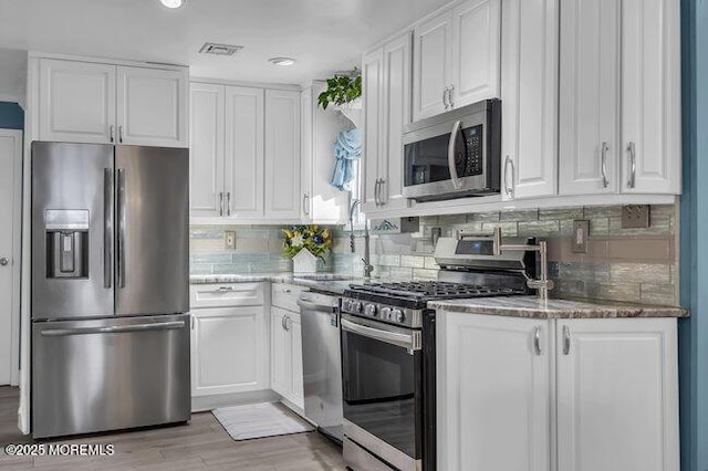 kitchen with stainless steel appliances, white cabinetry, backsplash, and dark stone counters