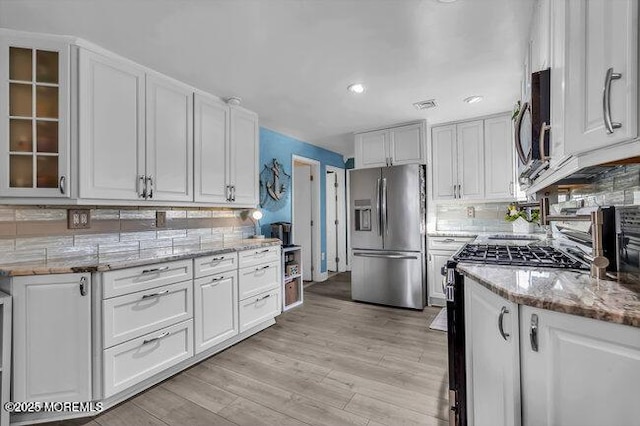 kitchen with appliances with stainless steel finishes, white cabinetry, light stone counters, decorative backsplash, and light wood-type flooring