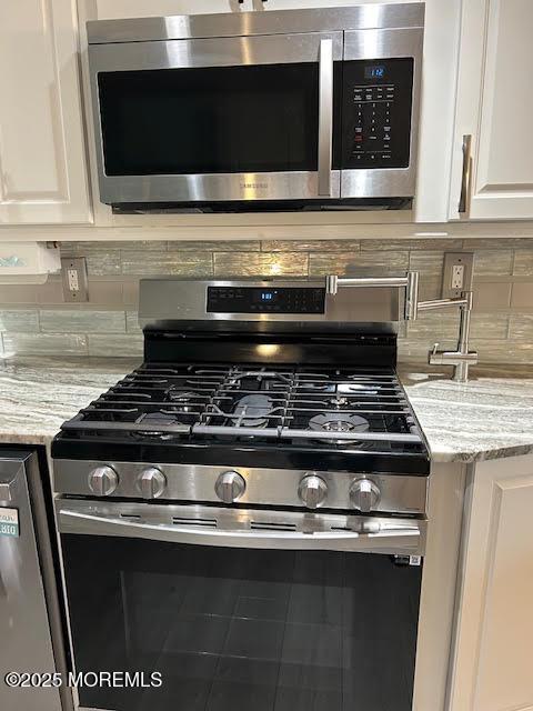 room details featuring stainless steel appliances, light stone countertops, white cabinets, and decorative backsplash