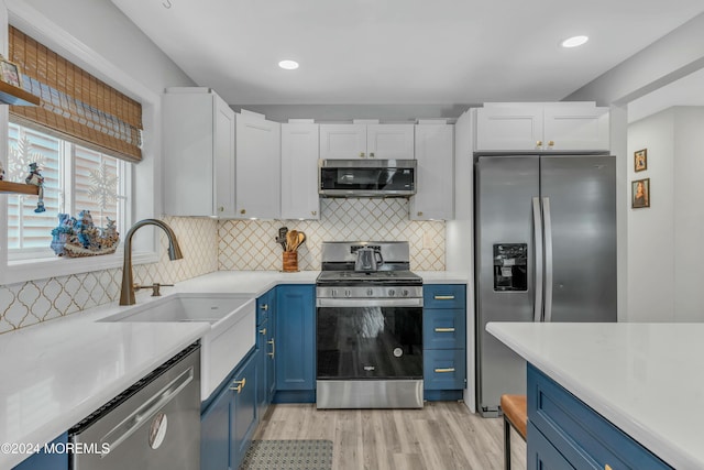 kitchen featuring appliances with stainless steel finishes, backsplash, blue cabinets, sink, and white cabinetry