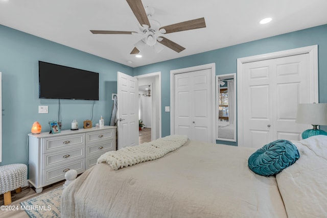 bedroom with hardwood / wood-style flooring, ceiling fan, and multiple closets