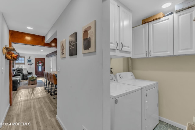 clothes washing area featuring washer and dryer, light hardwood / wood-style flooring, and cabinets