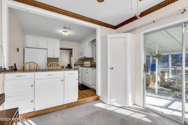 kitchen featuring light carpet, dark stone counters, white appliances, crown molding, and white cabinets