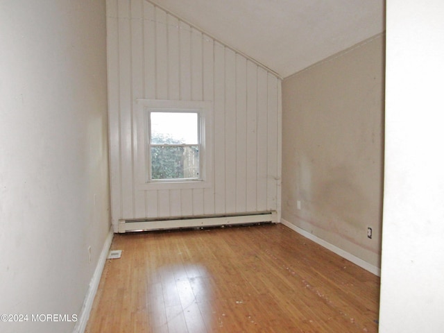 empty room featuring lofted ceiling, light wood-type flooring, wooden walls, and a baseboard heating unit