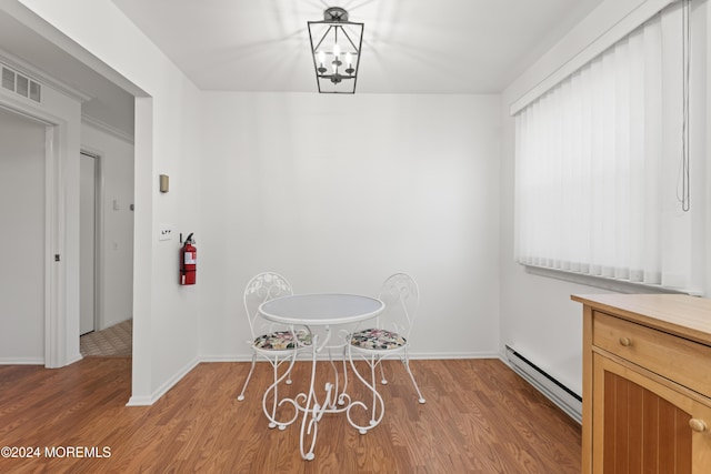 unfurnished dining area with hardwood / wood-style floors, a chandelier, and a baseboard heating unit