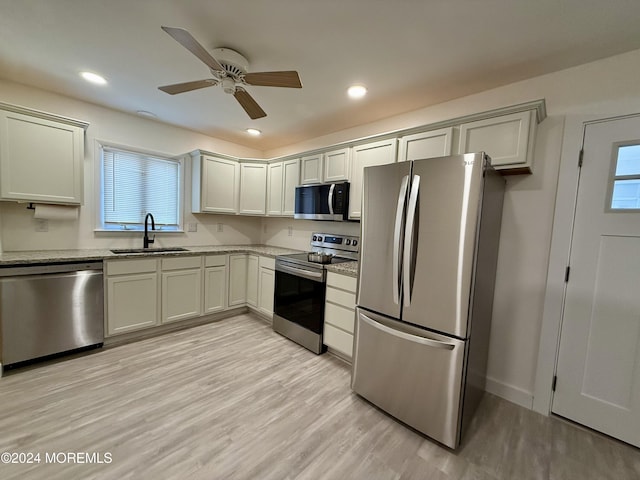 kitchen with appliances with stainless steel finishes, sink, ceiling fan, light stone countertops, and light wood-type flooring