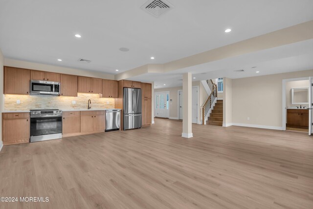 kitchen with light wood-style flooring, backsplash, open floor plan, appliances with stainless steel finishes, and light countertops