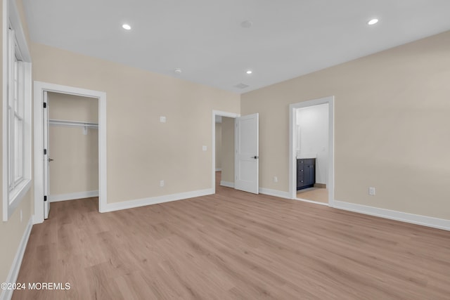 unfurnished bedroom featuring ensuite bathroom, light hardwood / wood-style floors, a walk in closet, and a closet