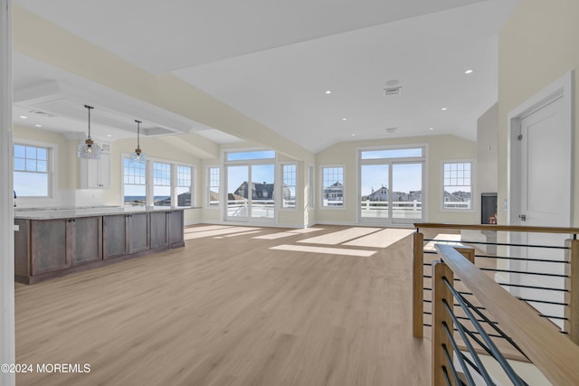 unfurnished living room featuring light hardwood / wood-style flooring, vaulted ceiling, plenty of natural light, and a notable chandelier