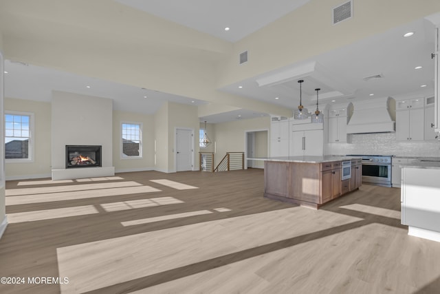 kitchen featuring light wood-type flooring, custom range hood, pendant lighting, white cabinets, and a large island