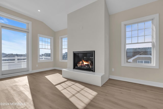 unfurnished living room featuring wood finished floors, baseboards, lofted ceiling, and a glass covered fireplace