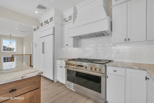 kitchen featuring white cabinets, high end appliances, custom range hood, and light wood-type flooring