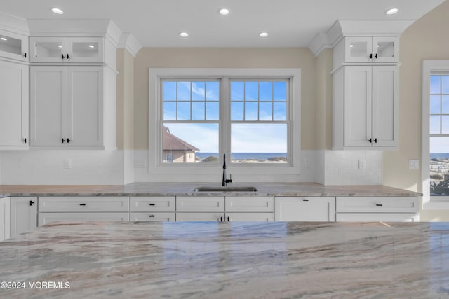 kitchen with white cabinets, backsplash, light stone countertops, and sink