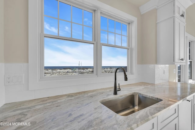 kitchen with light stone counters, white cabinetry, and sink